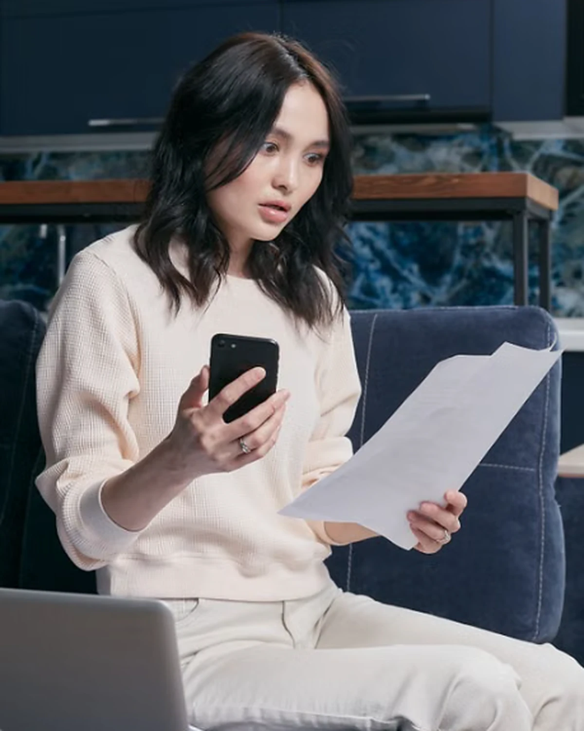 Woman reviewing financial information on her smartphone beside a laptop.