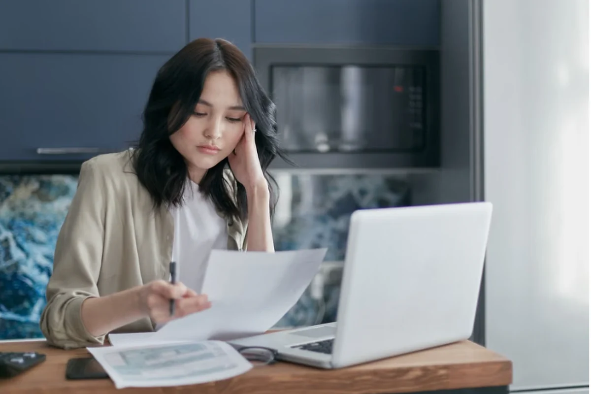Woman reviewing financial documents beside a laptop.